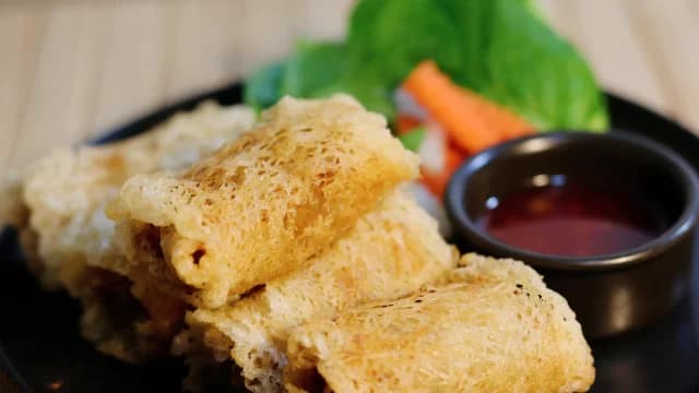 Golden spring rolls with a dipping sauce and fresh vegetables.